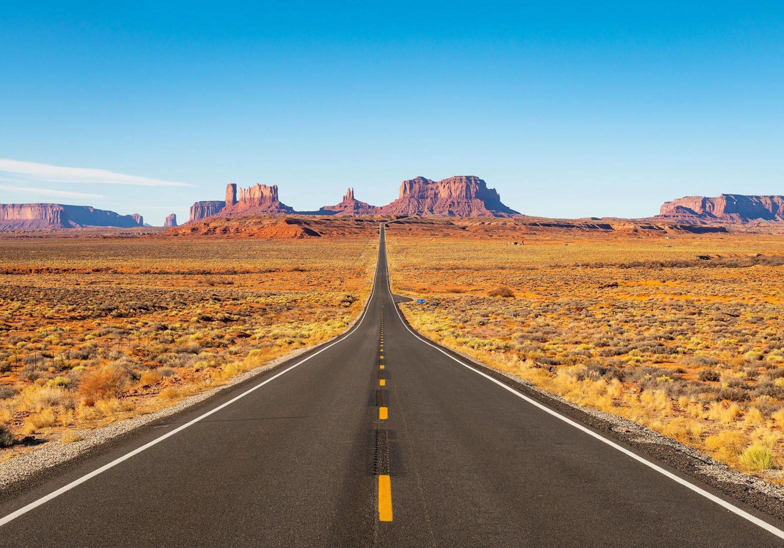 Straight desert highway toward red rock mesas